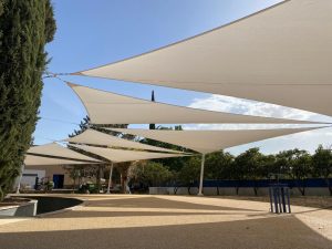 a white shade structure with trees and a blue sky